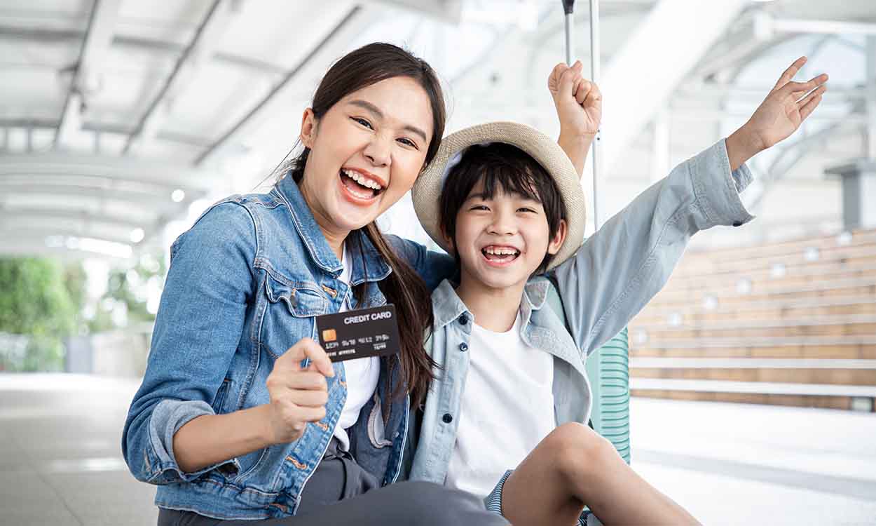 Duas pessoas comemorando com um cartão de crédito a mão. Elas parecem mãe e filho