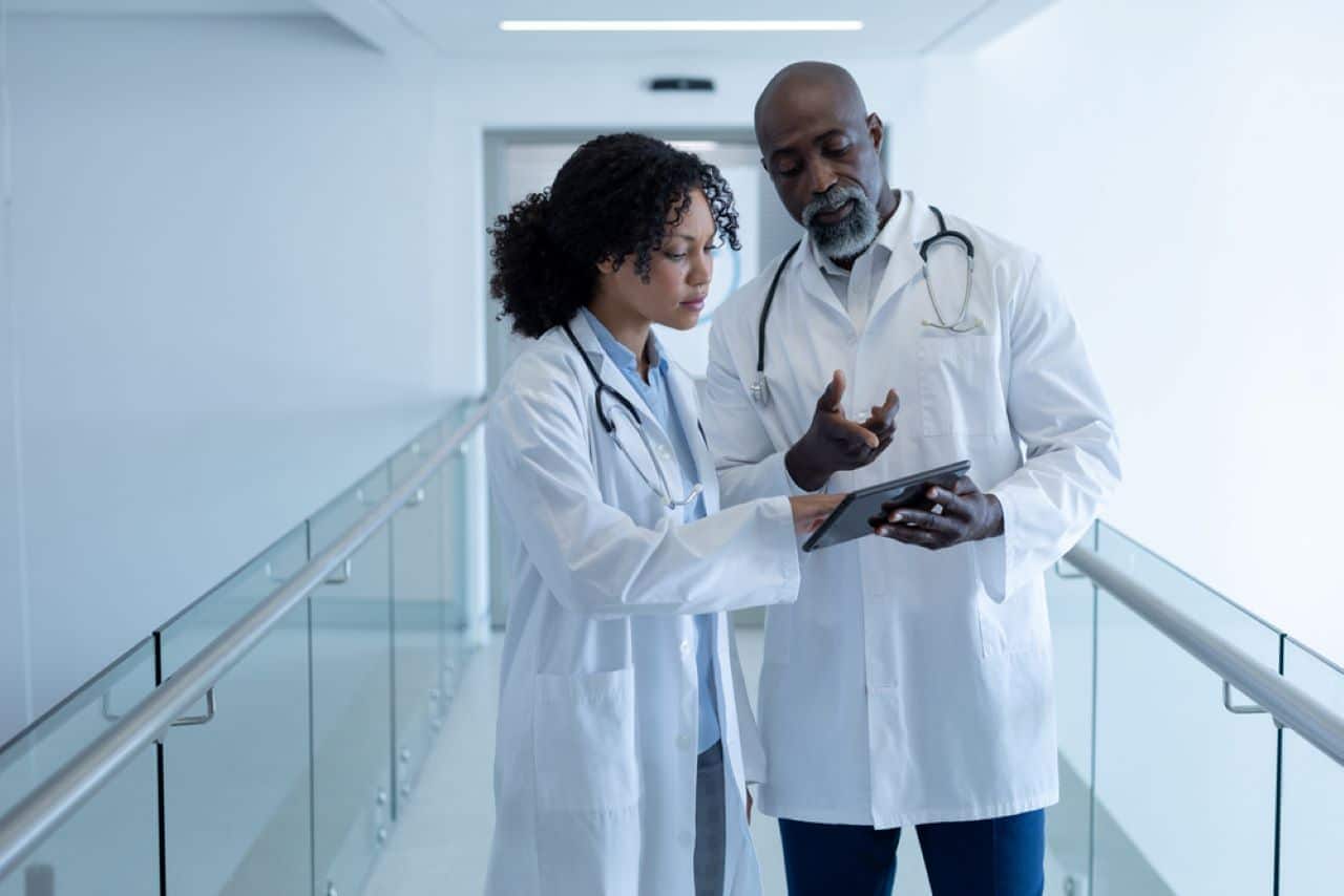 Um médico e uma médica olhando para um tablet no corredor de um hospital