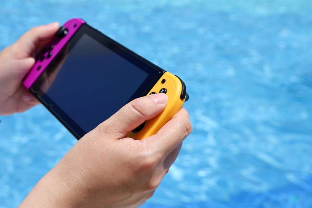 menino brincando com mini videogame portátil, ao fundo tem uma piscina