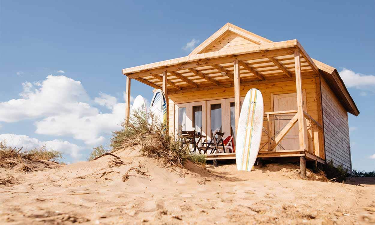 Casa de madeira na areia com um prancha de surfe em frente