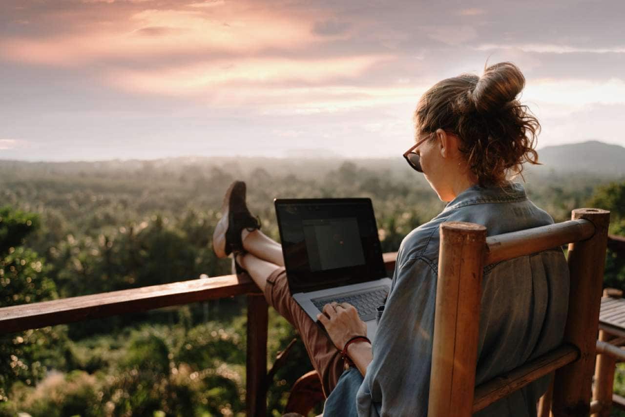 Mulher branca de coque usando o notebook fazendo trabalho remoto na varanda de sua casa.