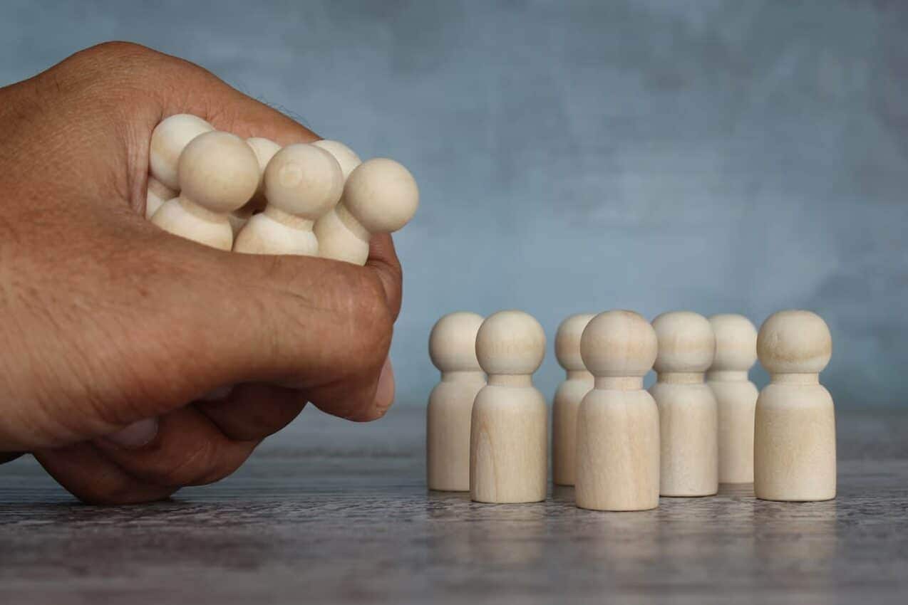 peças de miniatura representando grupo de trabalhadores e mão retirando parte das peças, representando uma demissão em massa lojas