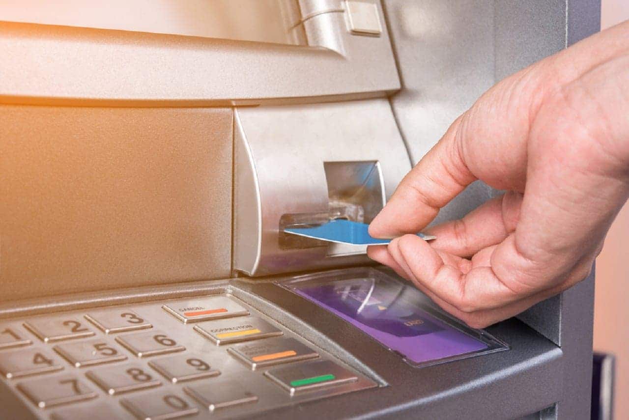 Imagem de uma mão inserindo um cartão azul em um caixa eletrônico