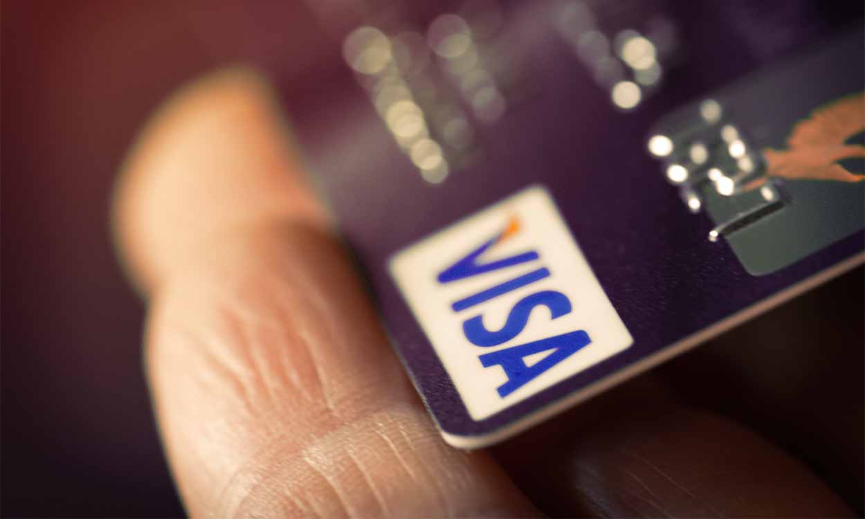 Pessoa segurando um cartão e a bandeira Visa está em foco.