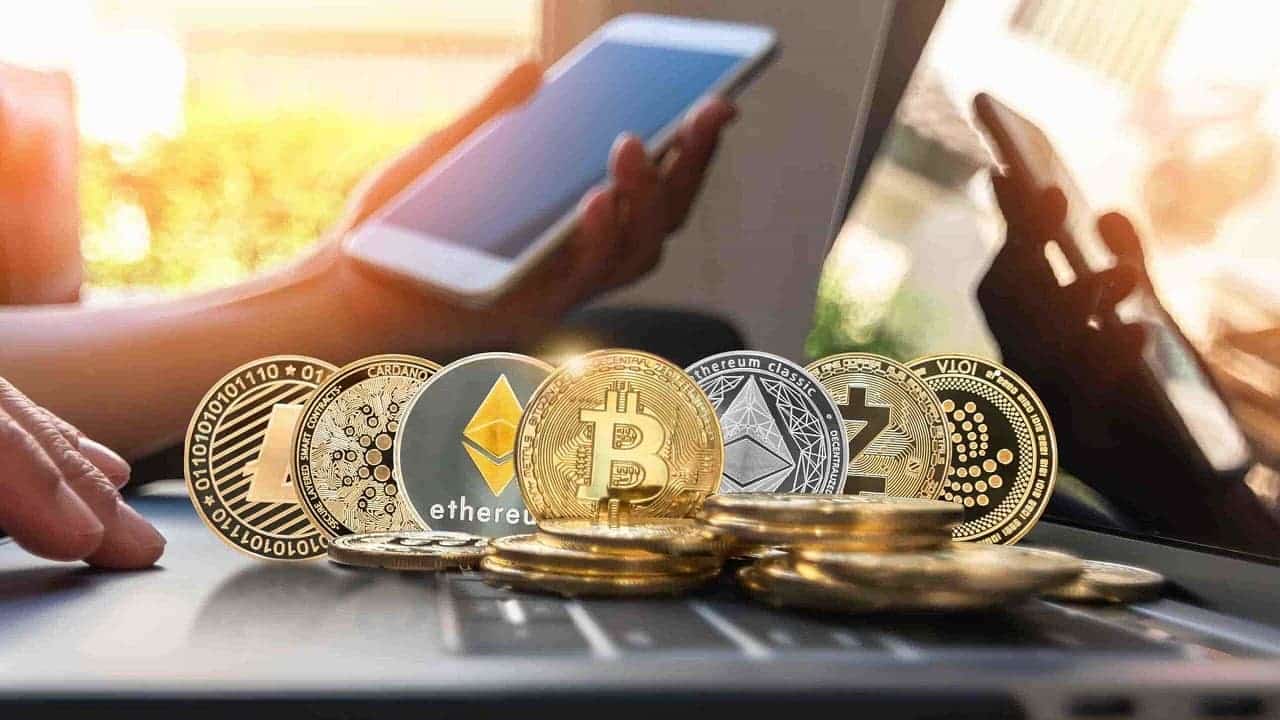 uma pessoa usando celular ao lado de várias criptomoedas em cima de notebook