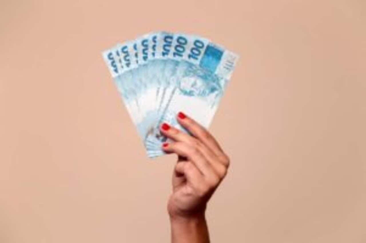 Imagem de uma mão segurando diversas notas de R$100