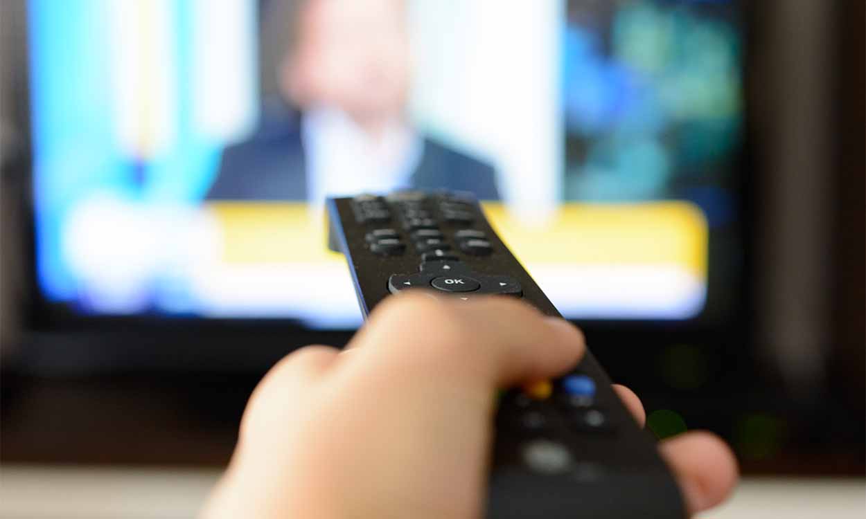 Mão segurando controle apontando para televisão.