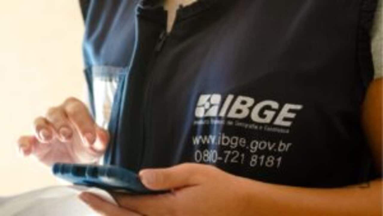 Recenseador com colete do IBGE segurando dispositivo de coleta de informações do Censo