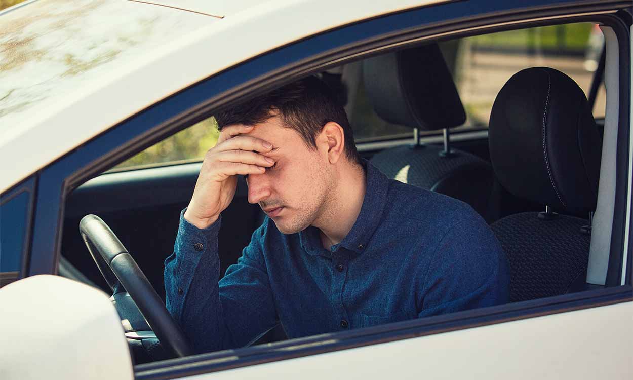 Homem dentro do carro com a mão na cabeça preocupado com instensa fiscalização e possibilidade de multa.