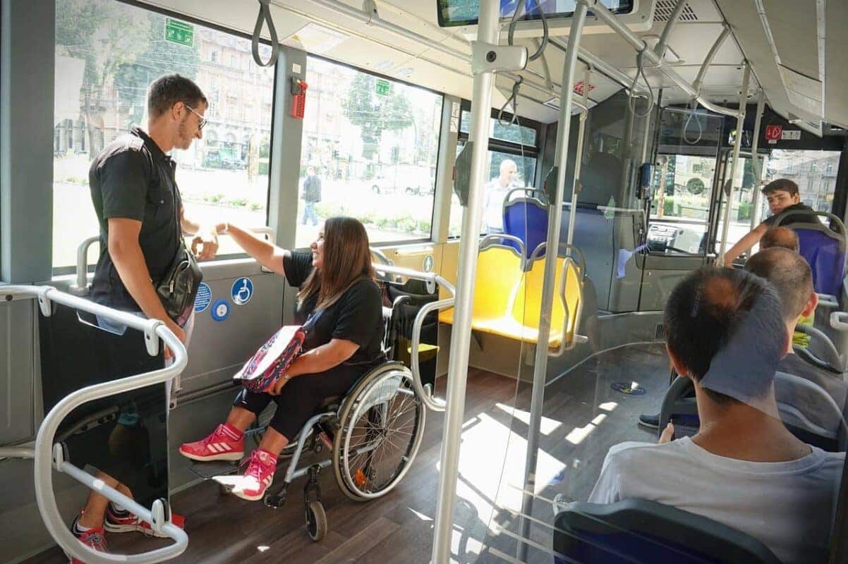 Uma mulher cadeirante viajando em um ônibus, enquanto conversa com outro passageiro. acompanhantes