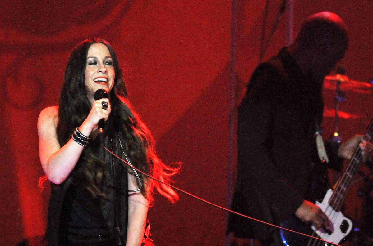 A cantora canadense Alanis Morissette cantando com microfone durante show.