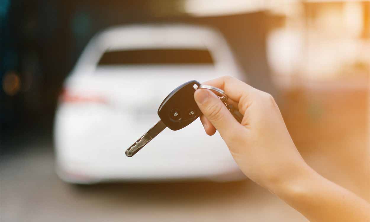 Pessoa com chave de veículo na mão e o mesmo estacionado à sua frente