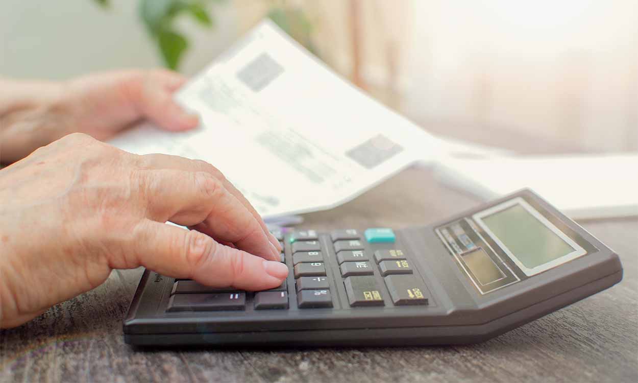 Idoso usando uma calculadora e segurando uma folha de papel