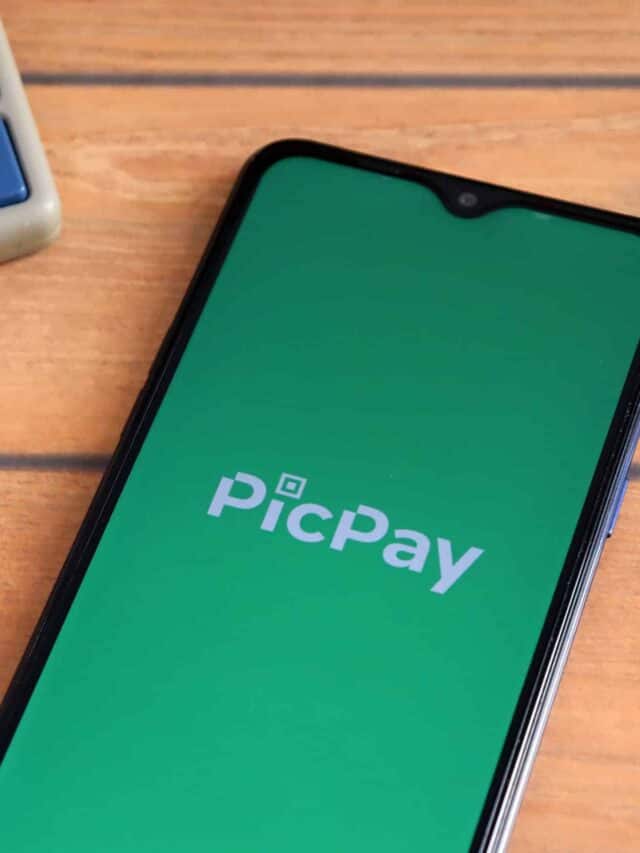 Aplicativo PicPay aberto no celular sobre uma mesa de madeira. À esquerda há um calculadora.