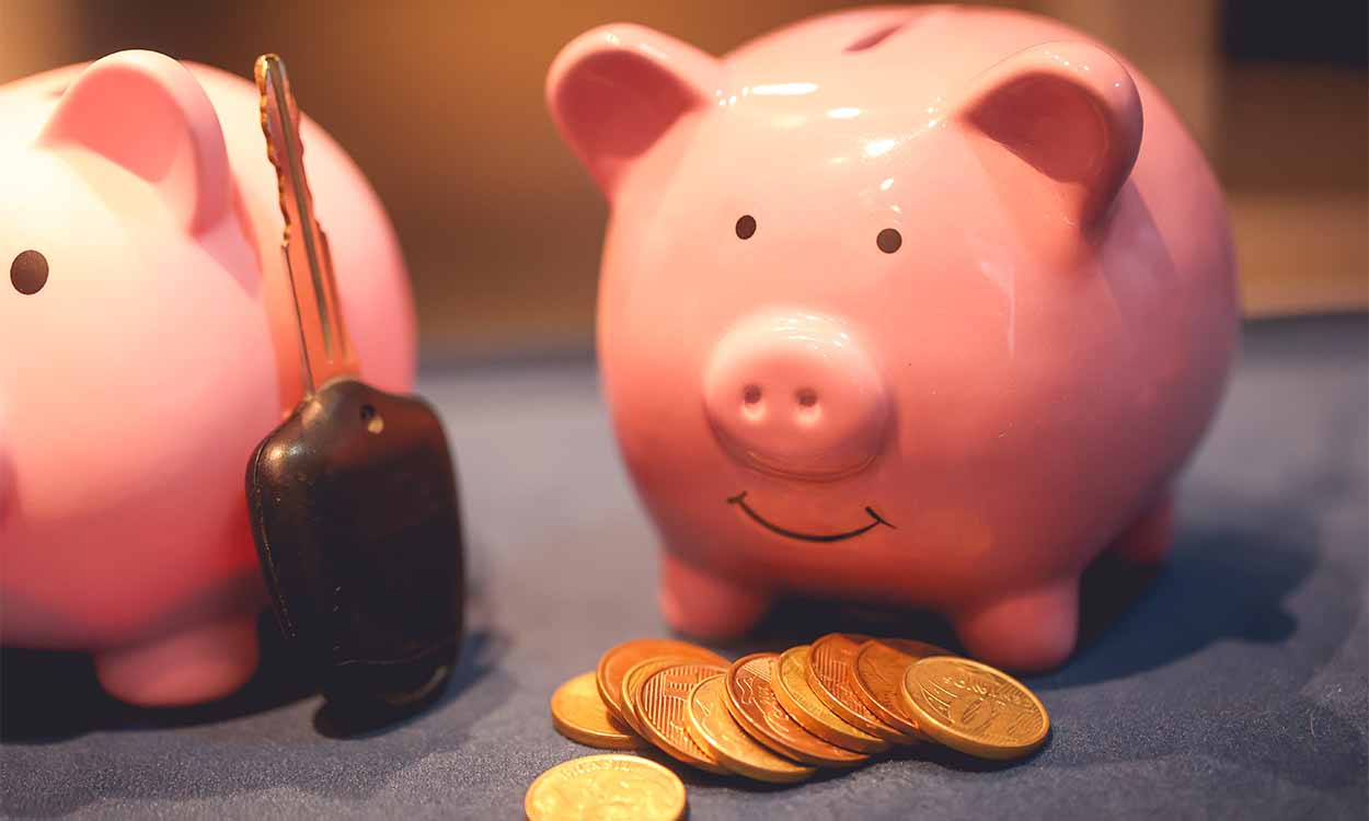 Porquinho cofre com moedas em frente e uma chave de carro apoiada ao lado