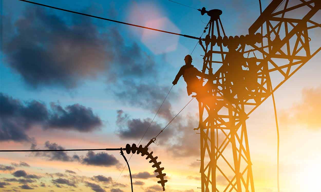 Imagem de postes de empresa de luz com um homem no alto de uma deles