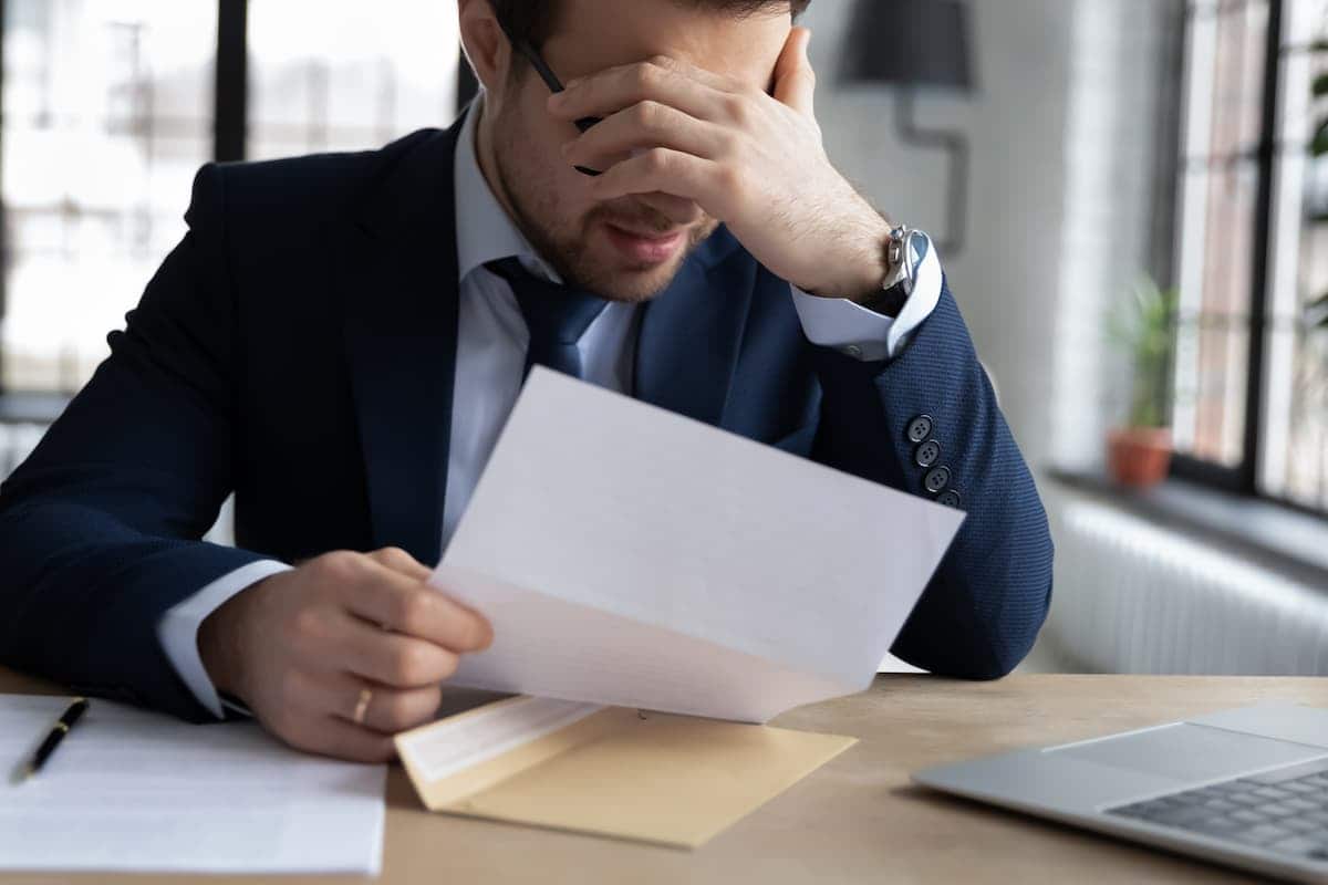 Funcionário de banco segurando uma folha de papel, com a mão tapando o rosto e um semblante de tristeza