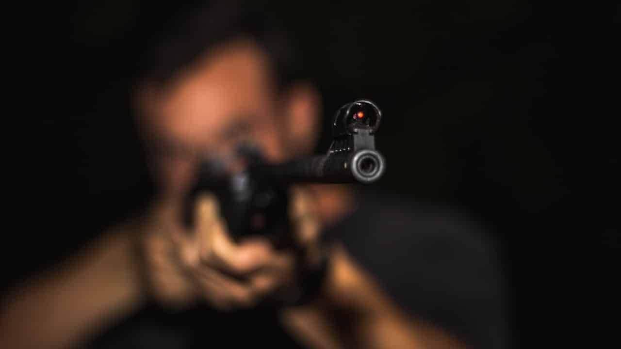 homem com rosto desfocado enquanto segura uma pistola apontada para a câmera