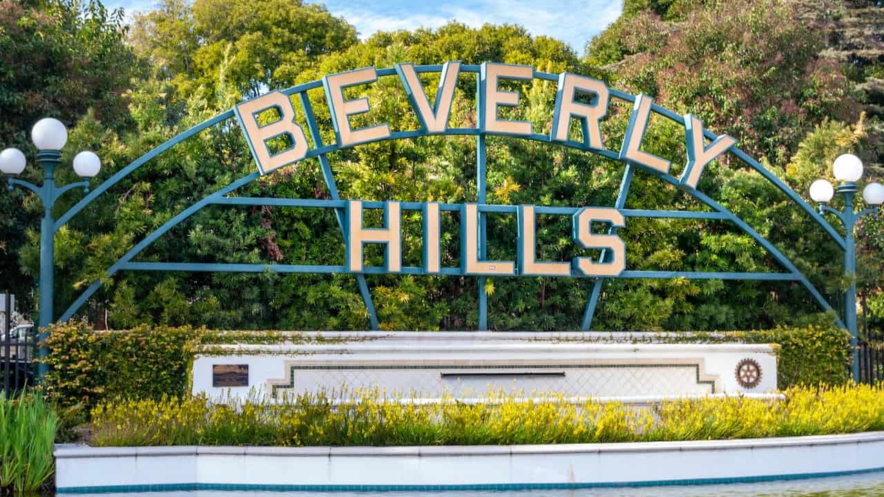Letreiro sofisticado escrito "Bervely Hills" no meio de árvores