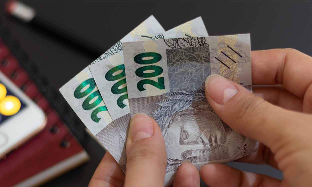 Foto mostra mão segurando notas de duzentos reais.