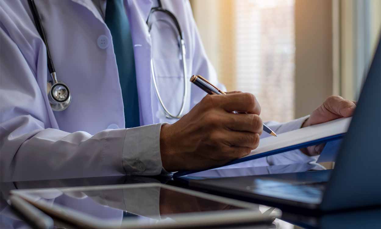 Médico com prancheta em frente ao computador