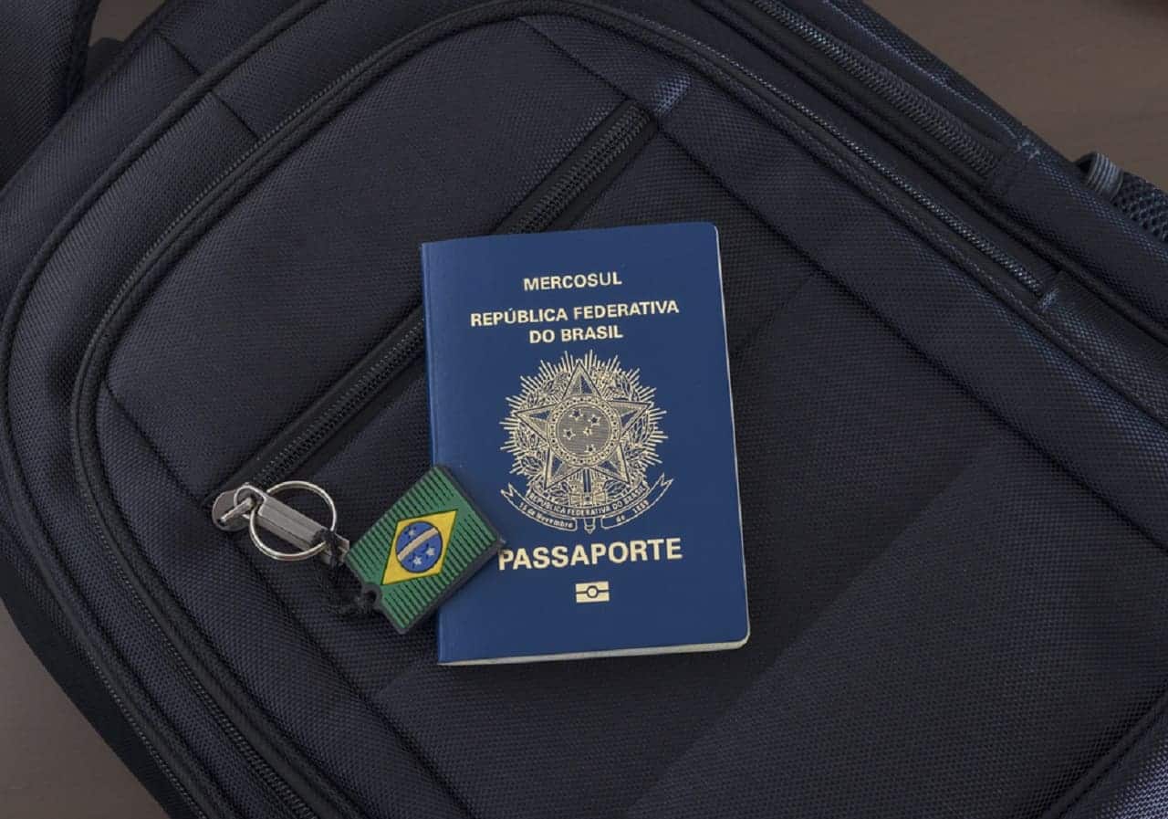 Imagem de um passaporte sob uma mochila com um chaveiro da bandeira do Brasil