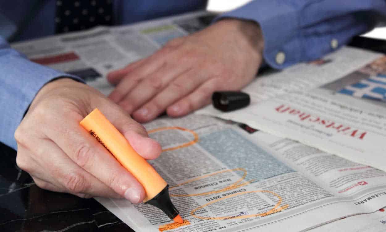 Pessoa circulando anúncios em um jornal, com um marcador de texto laranja