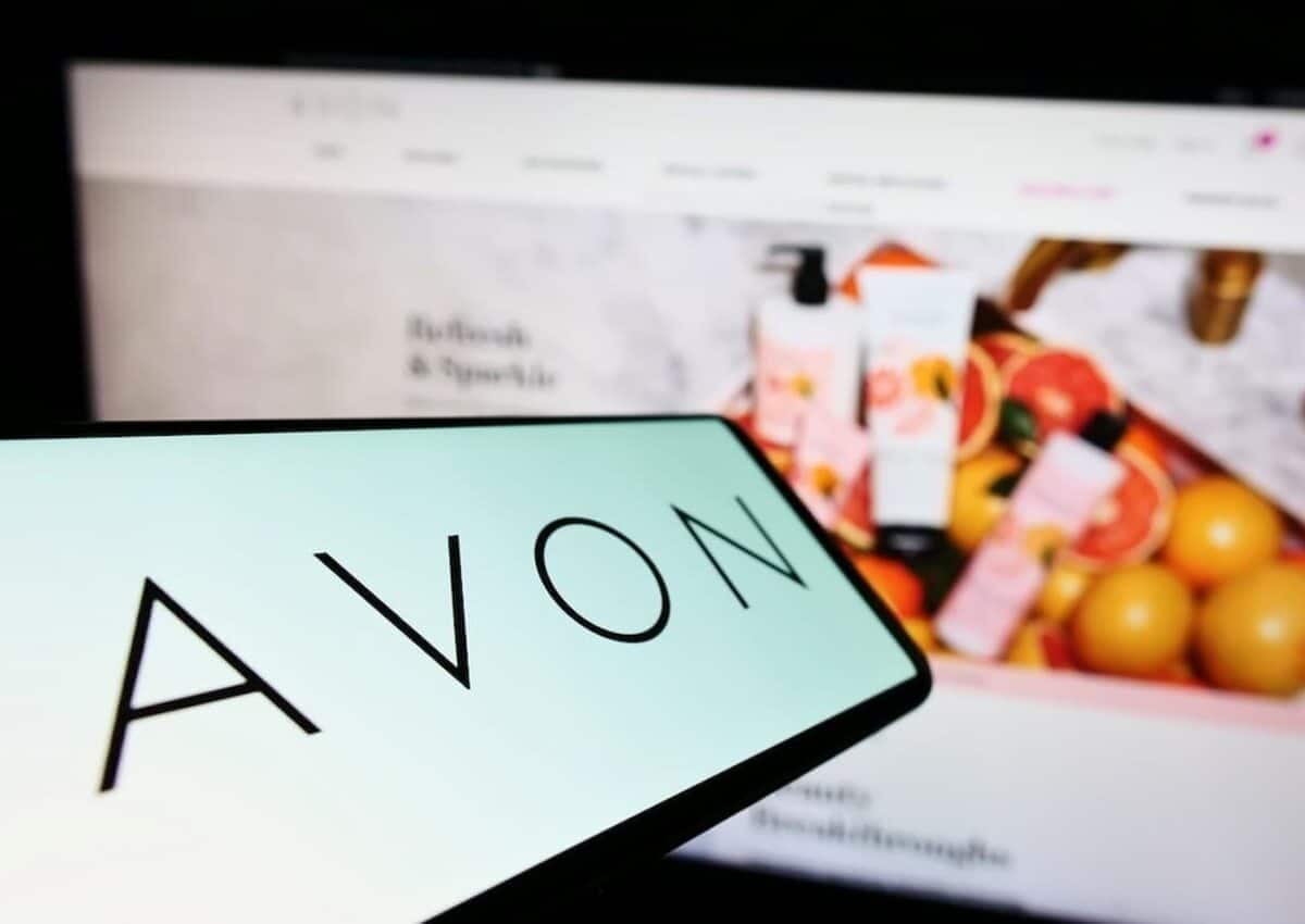 Na imagem, celular com o logo da Avon na tela e atrás um computador com o site aberto.