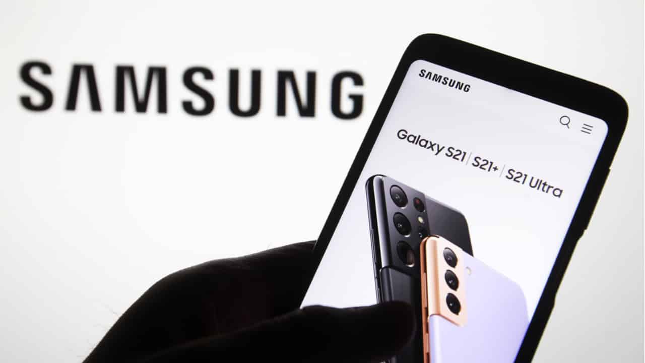 Logo da Samsung ao fundo e uma mão segurando um celular da marca.