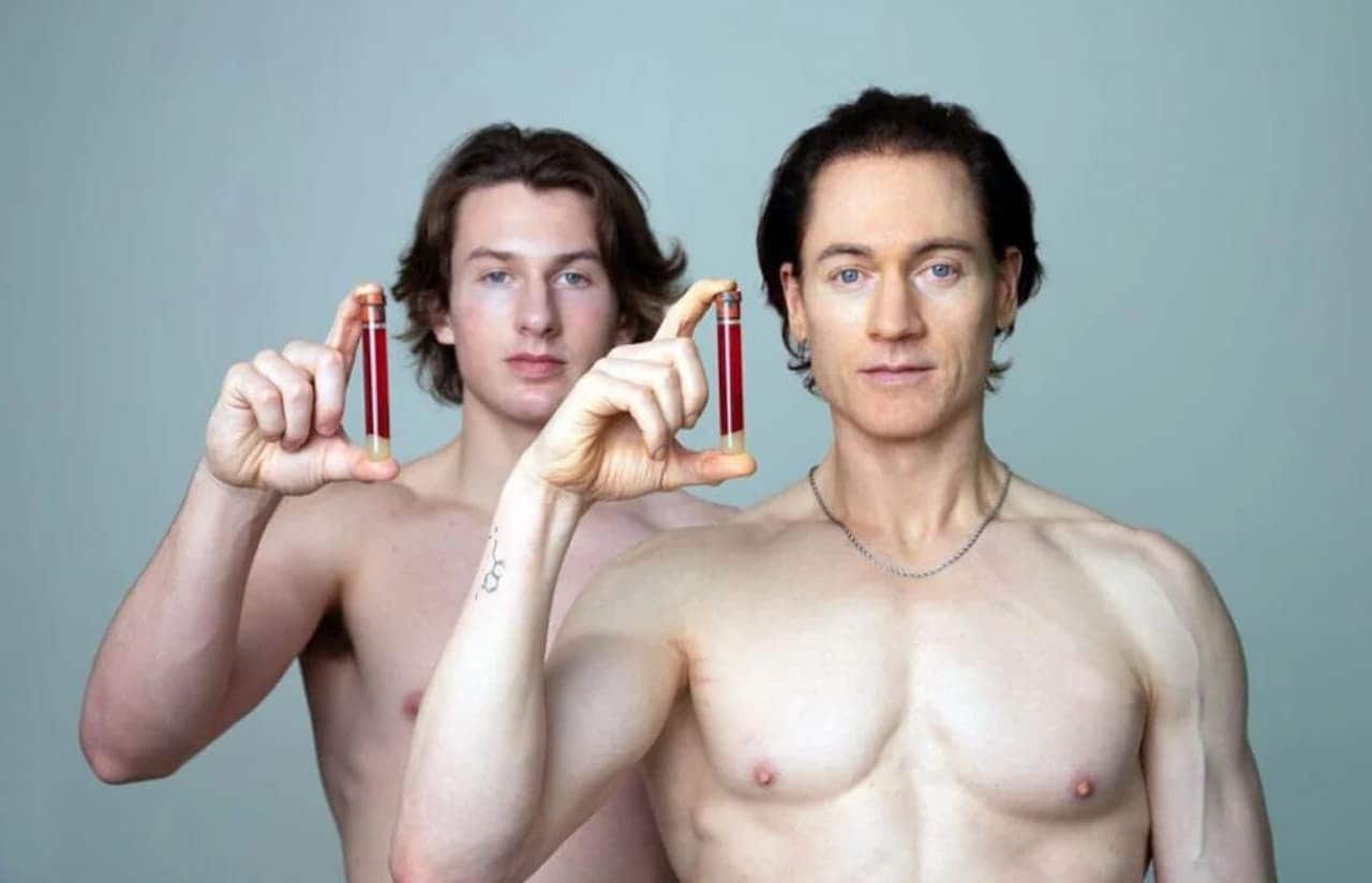 Bilionário Bryan Johnson e seu filho segurando tubos com amostras de plasmas. Os dois estão sem camisa.