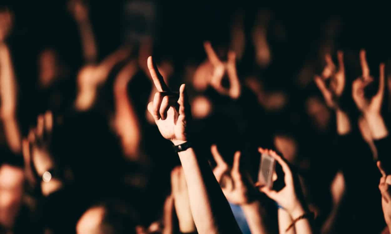 Pessoas curtindo um show de rock, fazendo sinal com as mãos