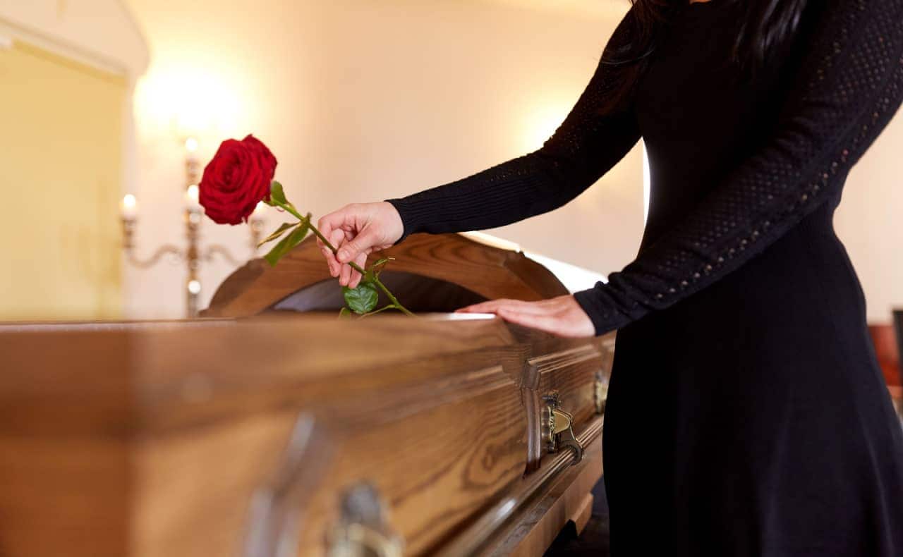 Caixão semi aberto com mulher de preto colocando uma rosa dentro