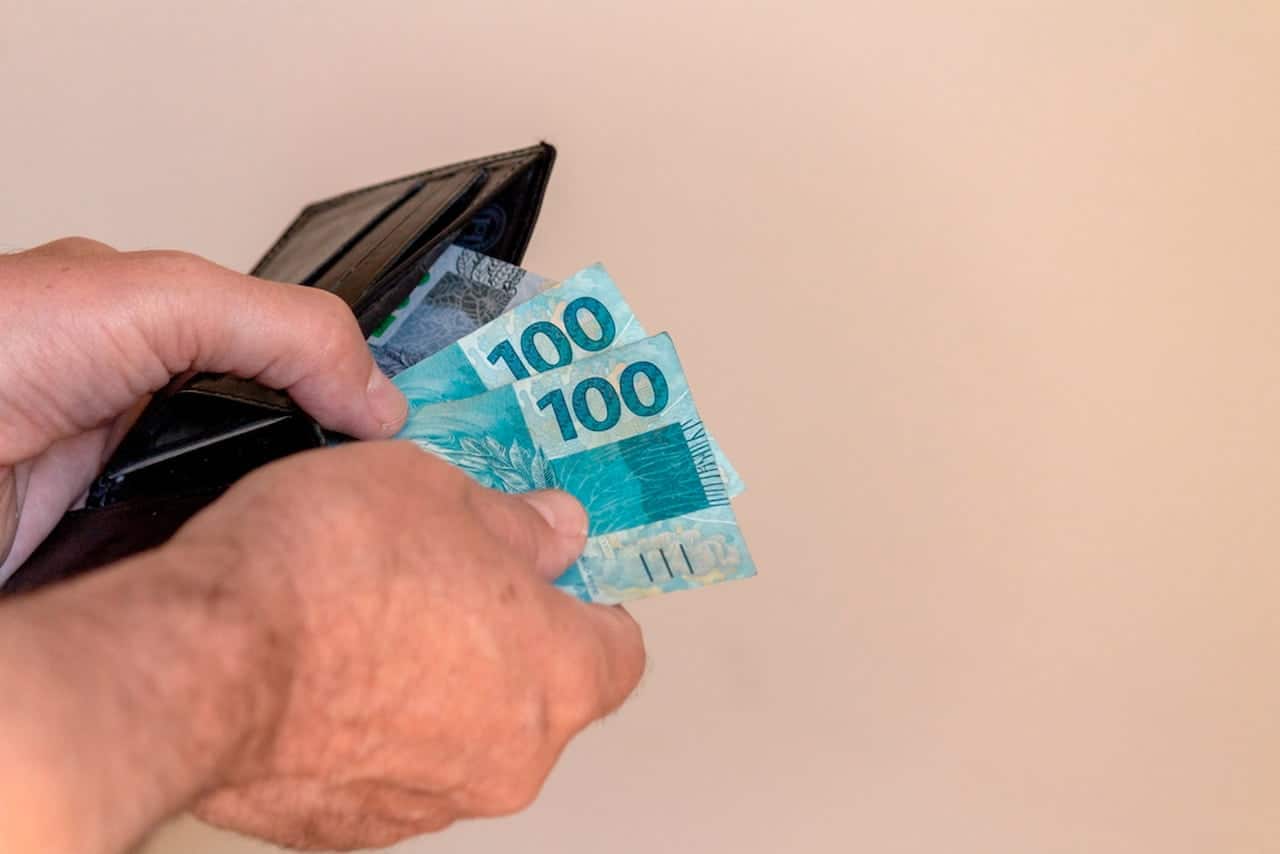 Mão retirando notas de 100 reais de uma carteira ipva