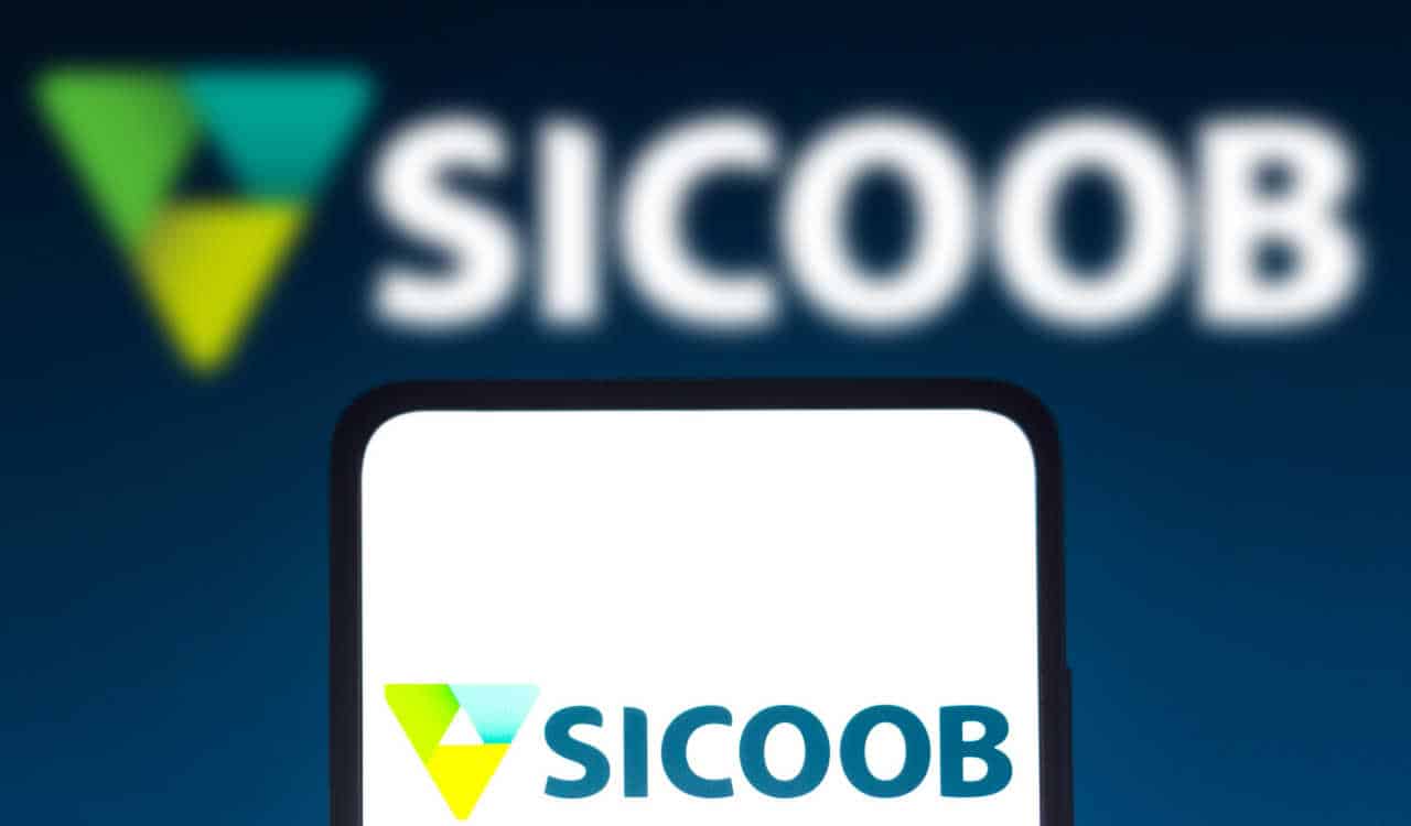 Celular com logo do Sicoob na tela e ao fundo, desfocado, outra logo da instituição