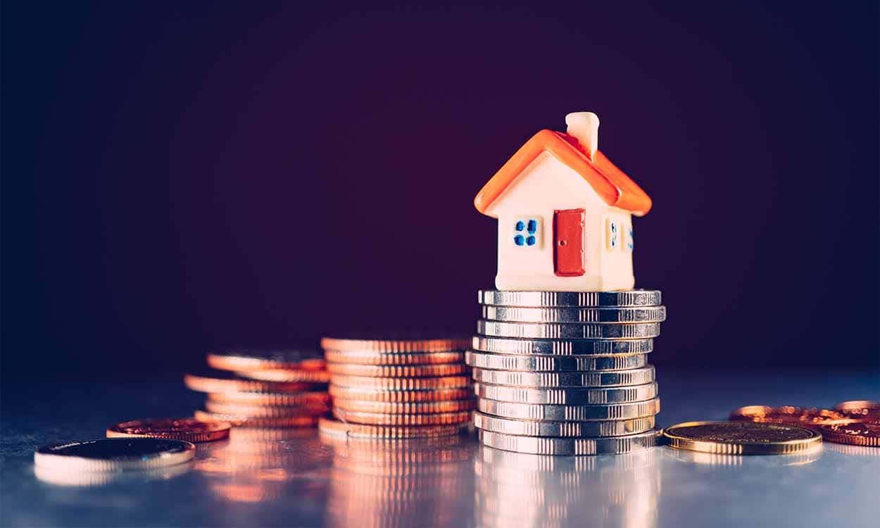 Miniatura de uma casa em cima de uma pilha de moedas