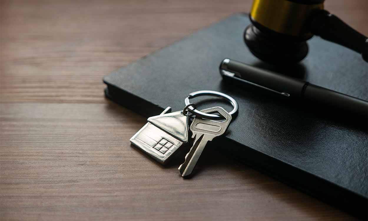 Martelo de juiz em cima de um caderno e ao lado de uma caneta e uma chave de casa