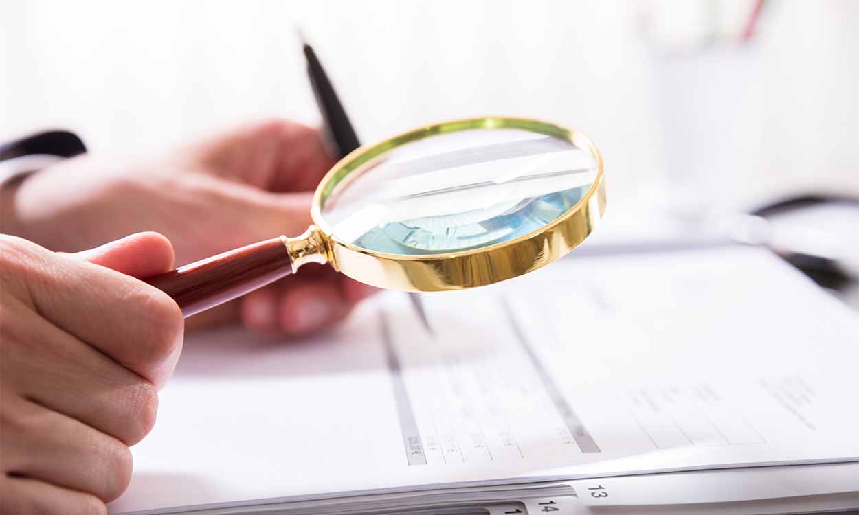 Pessoa segurando lupa olhando para documentos