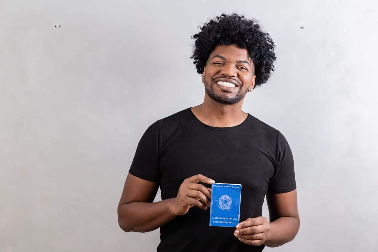 Homem sorrindo segurando carteira de trabalho.