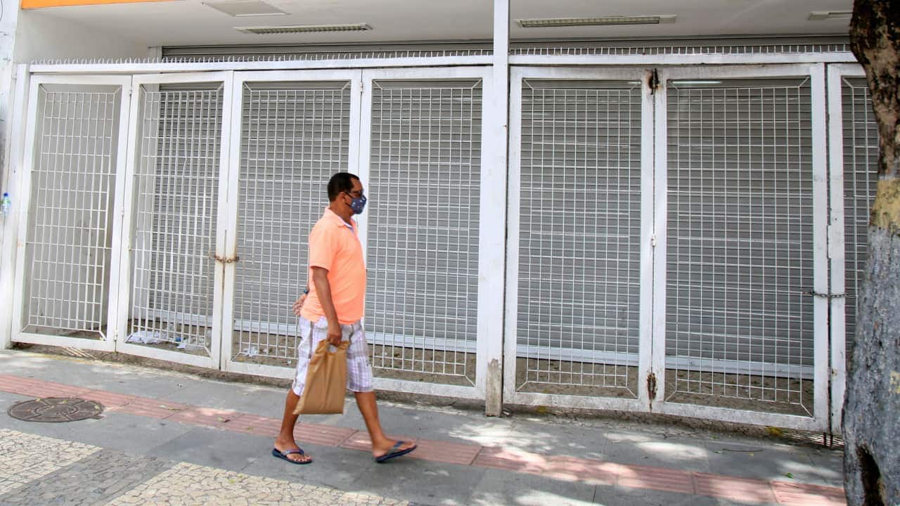Homem caminhando em frente à uma agência bancária fechada