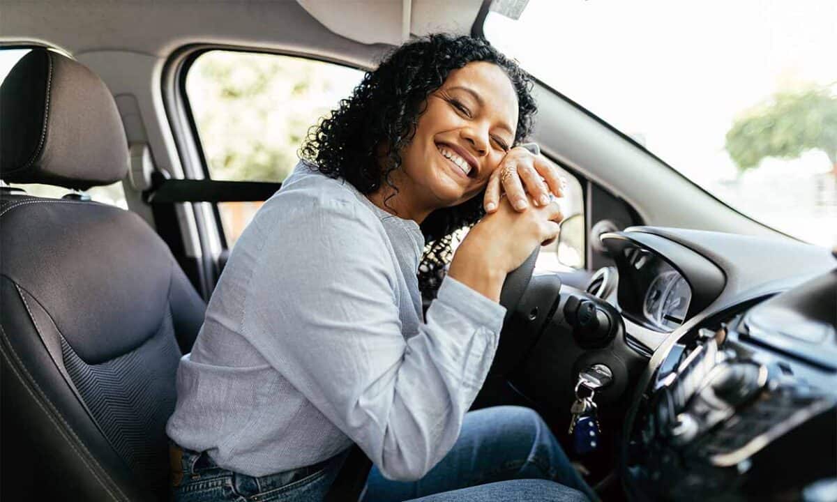 Mulher com expressão de felicidade dentro de um carro, abraçando o volante.