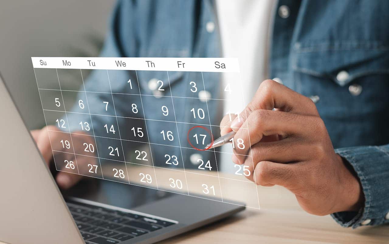 laptop e mão circulando sexta-feira em calendário 5º dia útil