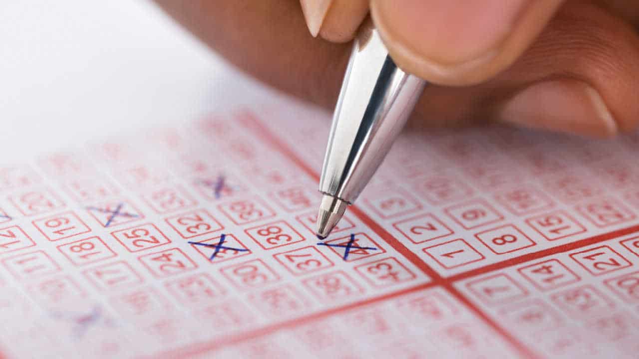 Mão apostando um número em um bilhete de loteria