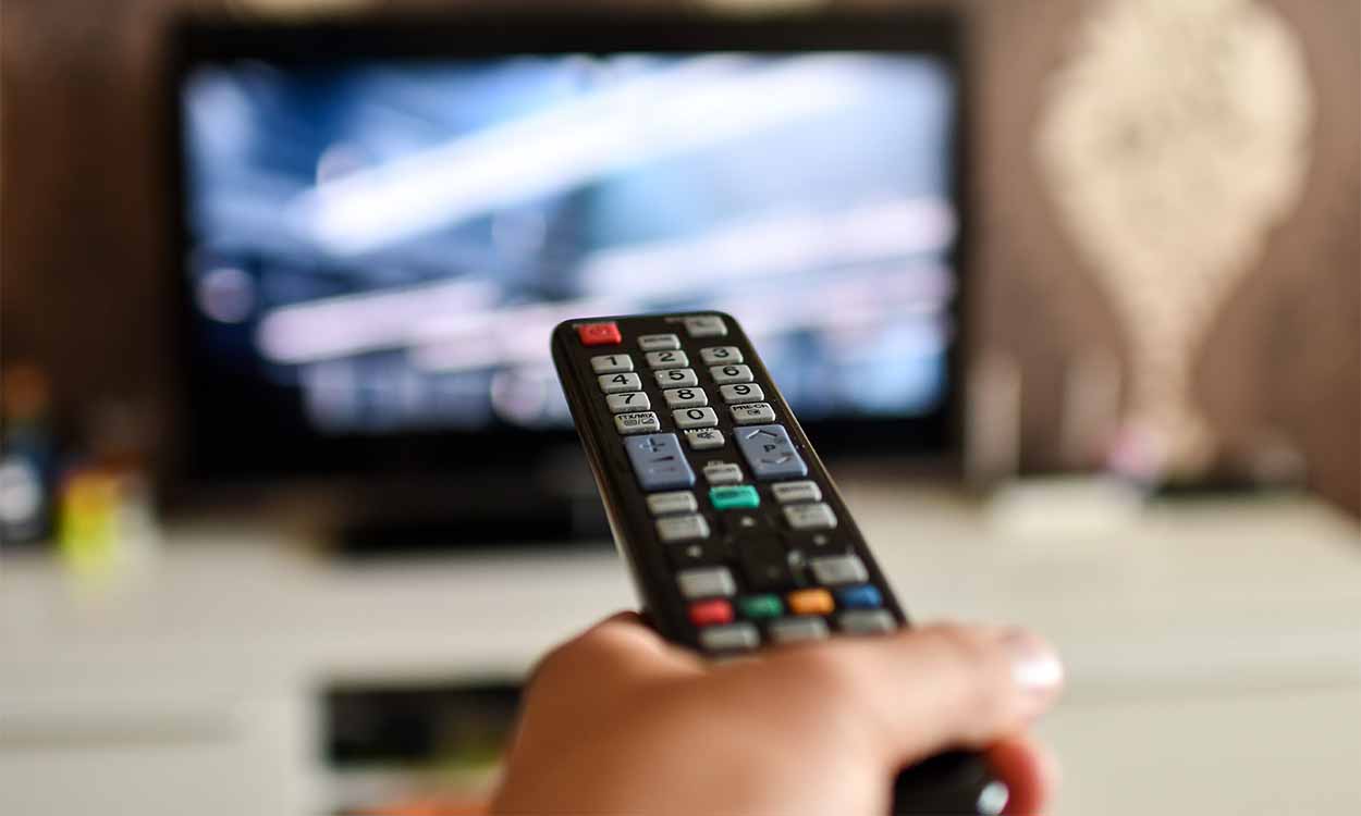Pessoa segurando um controle remoto e apontando para uma televisão ligada