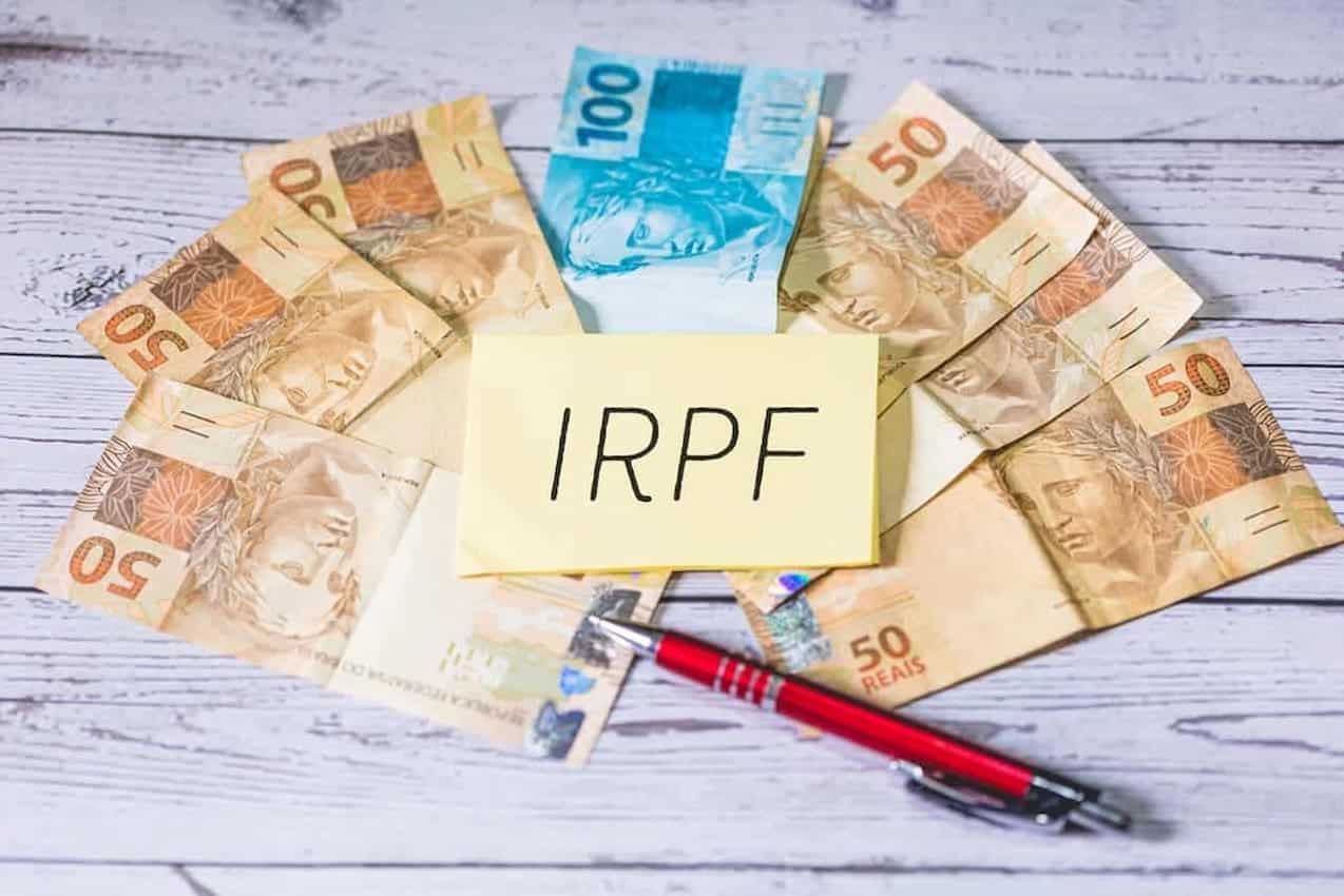 Papel com "IRPF" escrito e notas de dinheiro e caneta ao redor