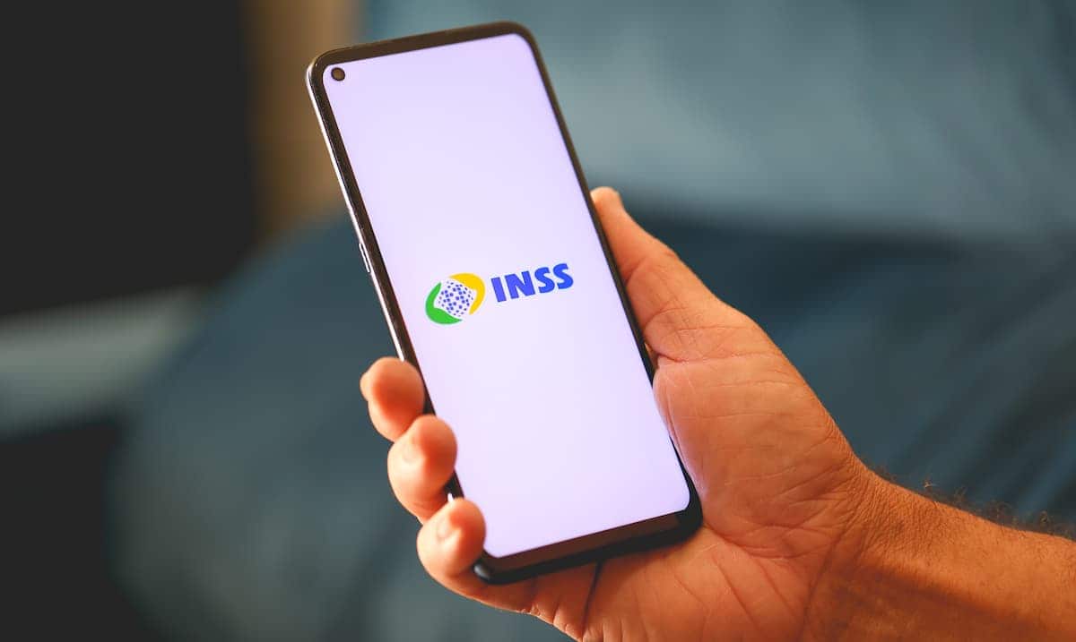 Mão segurando celular que exibe logo INSS.