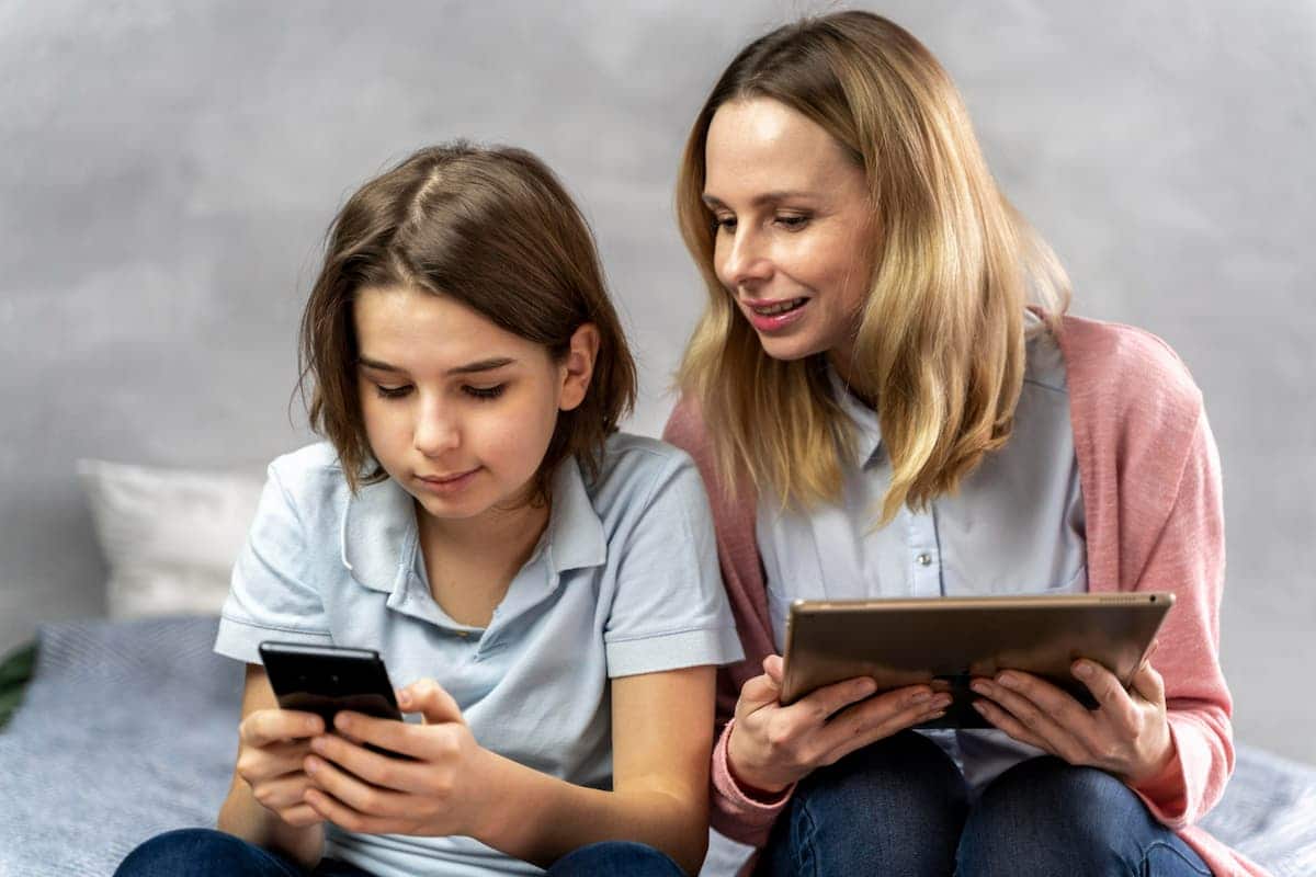 Mulher segurando um tablet e olhando a tela do celular de uma criança ao seu lado. adultização