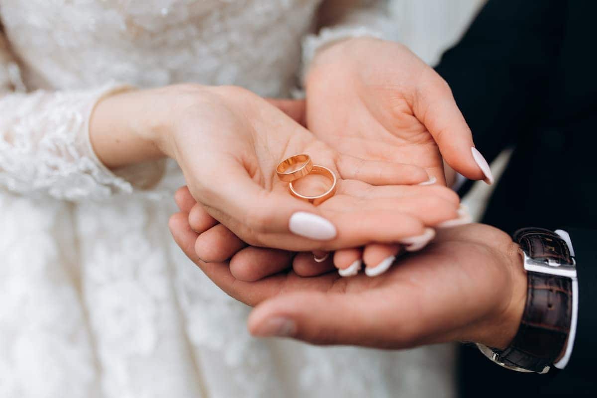 A imagem mostra um homem e uma mulher com as mãos juntas segurando um par de aliança. casar no civil auxílio casamento