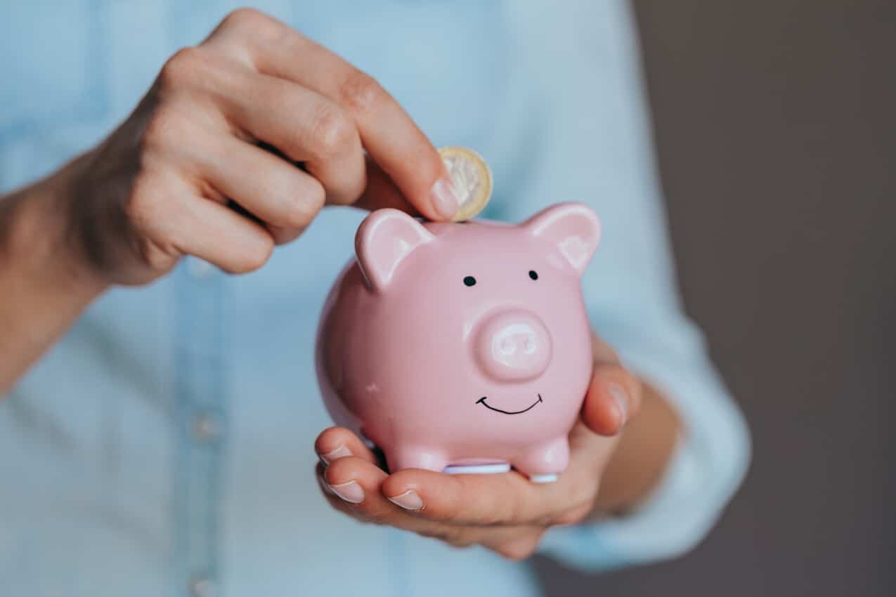 Na imagem, mão segurando cofre de porquinho e a outra depositando dinheiro ali. poupança premiada sicoob