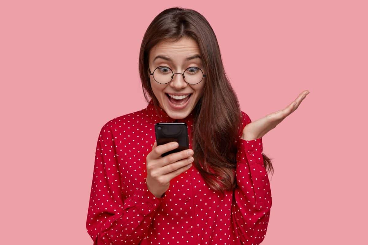 Mulher de óculos e blusa vermelha surpresa lendo notícia no celular