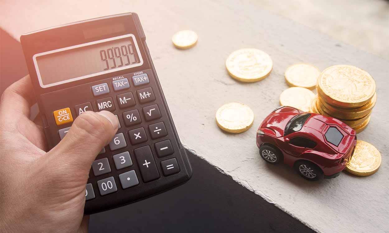 Pessoa segurando uma calculadora ao lado de uma miniatura de carro e várias moedas fazendo as contas para financiar um carro. financiamento